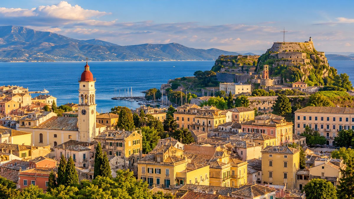 Panoramic view of Corfu Old Town, historic fortifications and the blue Ionian Sea at golden hour.