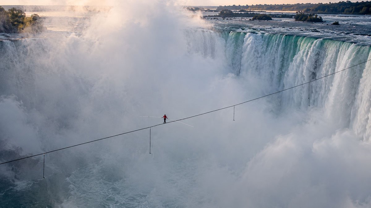 High-wire performer carrying a balancing pole above the mist-covered Horseshoe Falls at Niagara Falls.