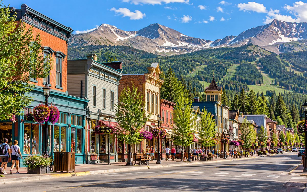 Historic Main Street in Breckenridge, Colorado, lined with colourful storefronts and flower planters against a Rocky Mountain backdrop.