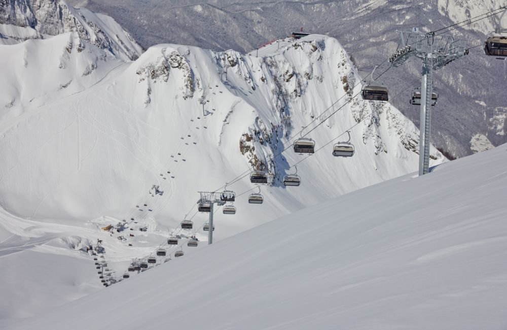 Gondola cable cars travelling over snow-covered ski slopes and rugged Caucasus mountain peaks at a ski resort near Sochi, Russia.