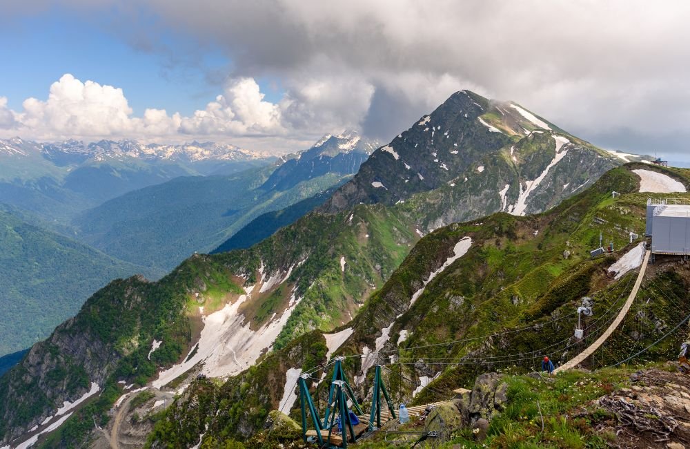 Panoramic view of Rosa Peak in Sochi National Park, Russia, showing rugged Caucasus mountain ridges, patches of snow and green valleys.
