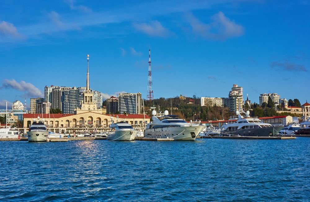Panoramic view of Sochi's Black Sea coastline, waterfront promenade and Caucasus mountains in the distance.