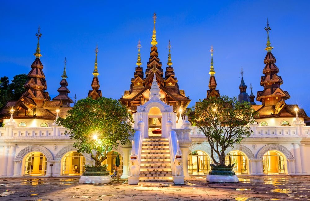 Ornate Lanna-style building in Chiang Mai, Thailand, illuminated at dusk with tiered wooden roofs, golden spires and a central staircase.