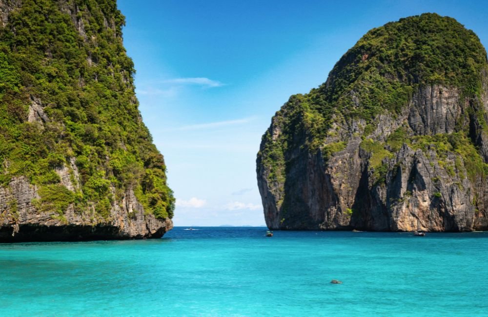 Towering limestone cliffs covered in tropical greenery rising above clear turquoise water in Krabi, Thailand.