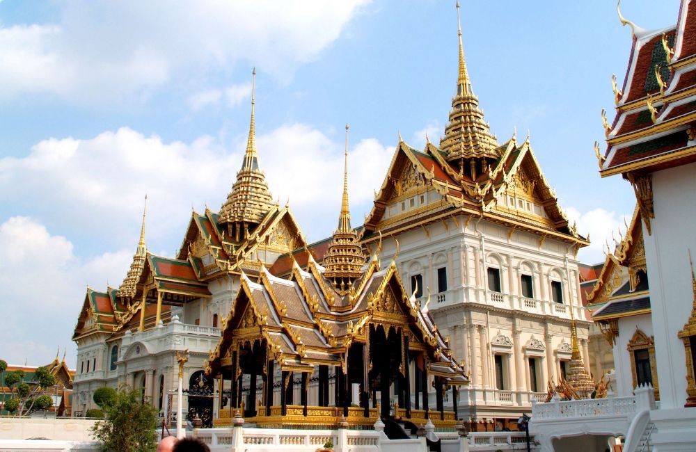 Ornate Thai architecture with golden spires, tiered roofs and white palace buildings at the Grand Palace complex in Bangkok, Thailand.