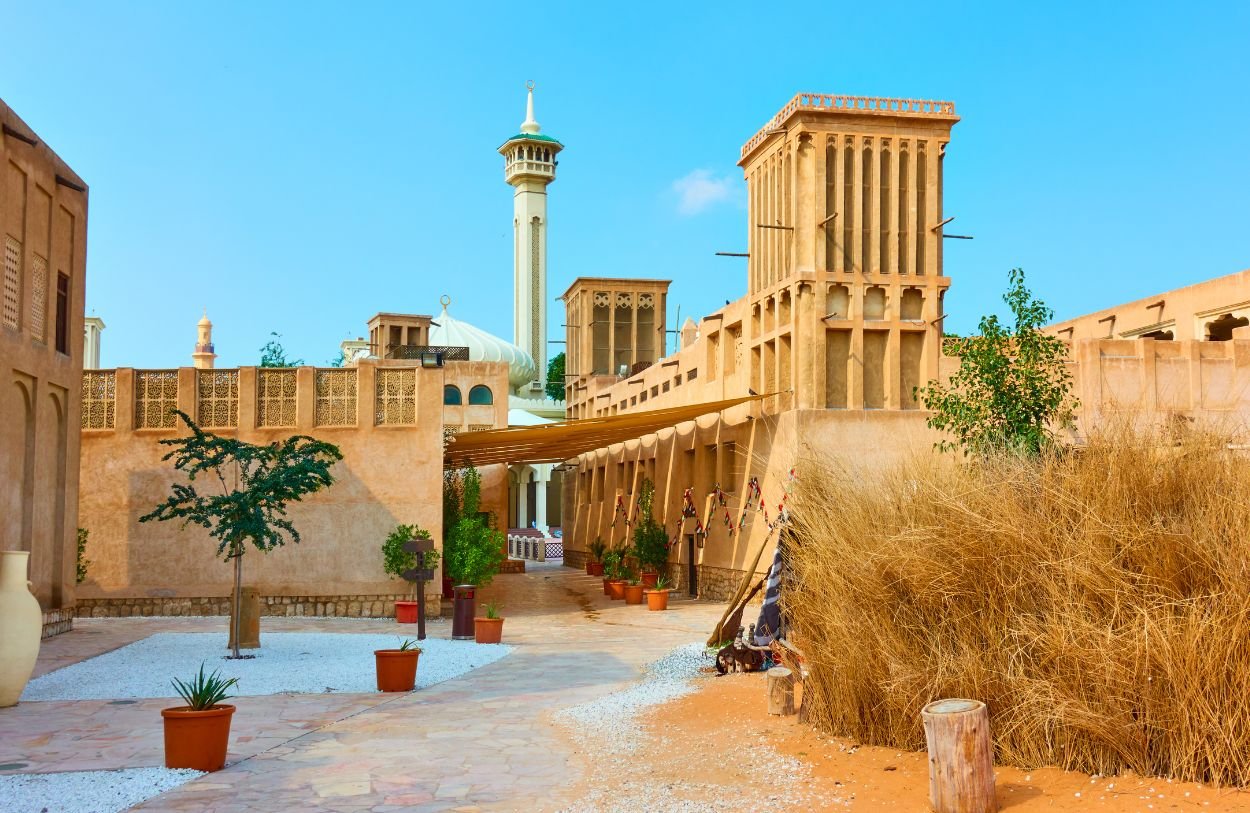 Traditional sand-coloured buildings and wind towers in Al Fahidi Historical Neighbourhood, Dubai, with a mosque minaret in the background