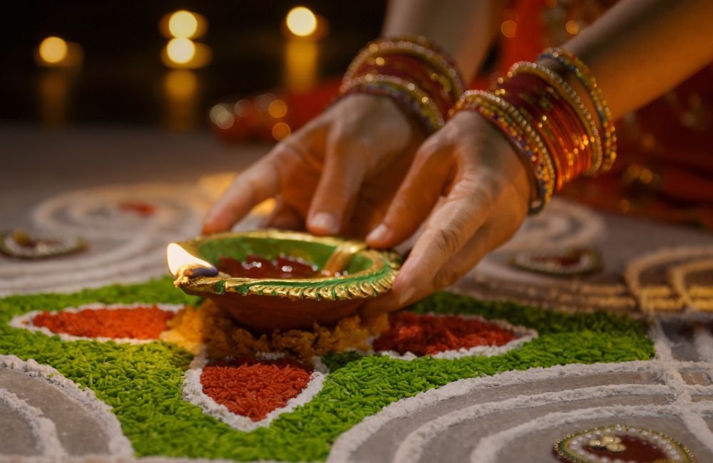 A woman placing a lit diya on a colourful rangoli during Diwali in India.